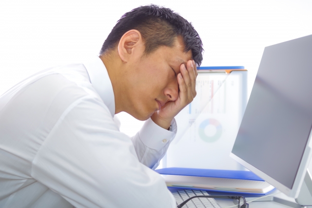 目の痛みを我慢してパソコン作業をする男性